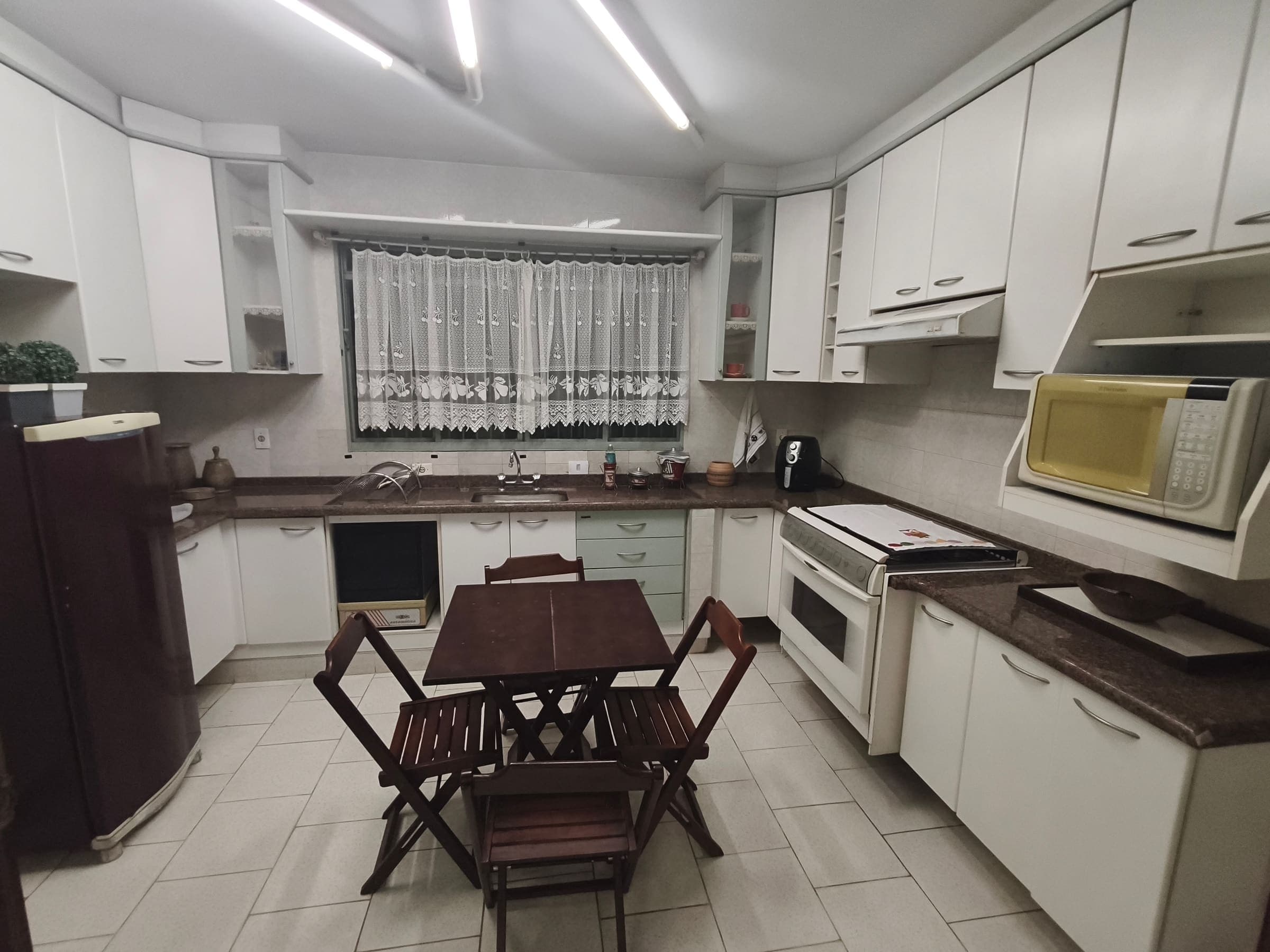 Cozinha com armários brancos de parede inteira, fogão, geladeira e mesa de apoio