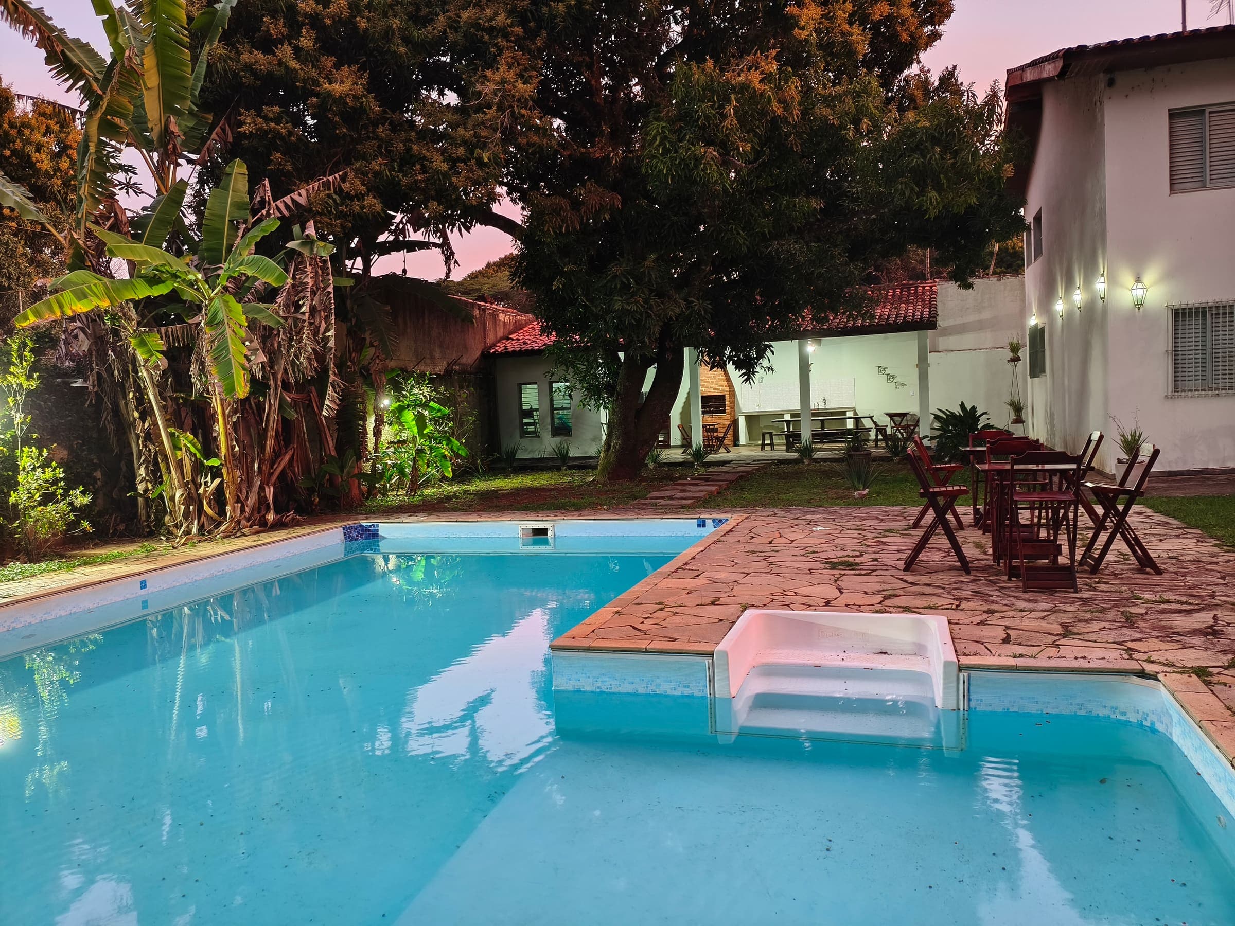 A piscina grande no fim do dia, com a casa e o céu cor-de-rosa ao fundo