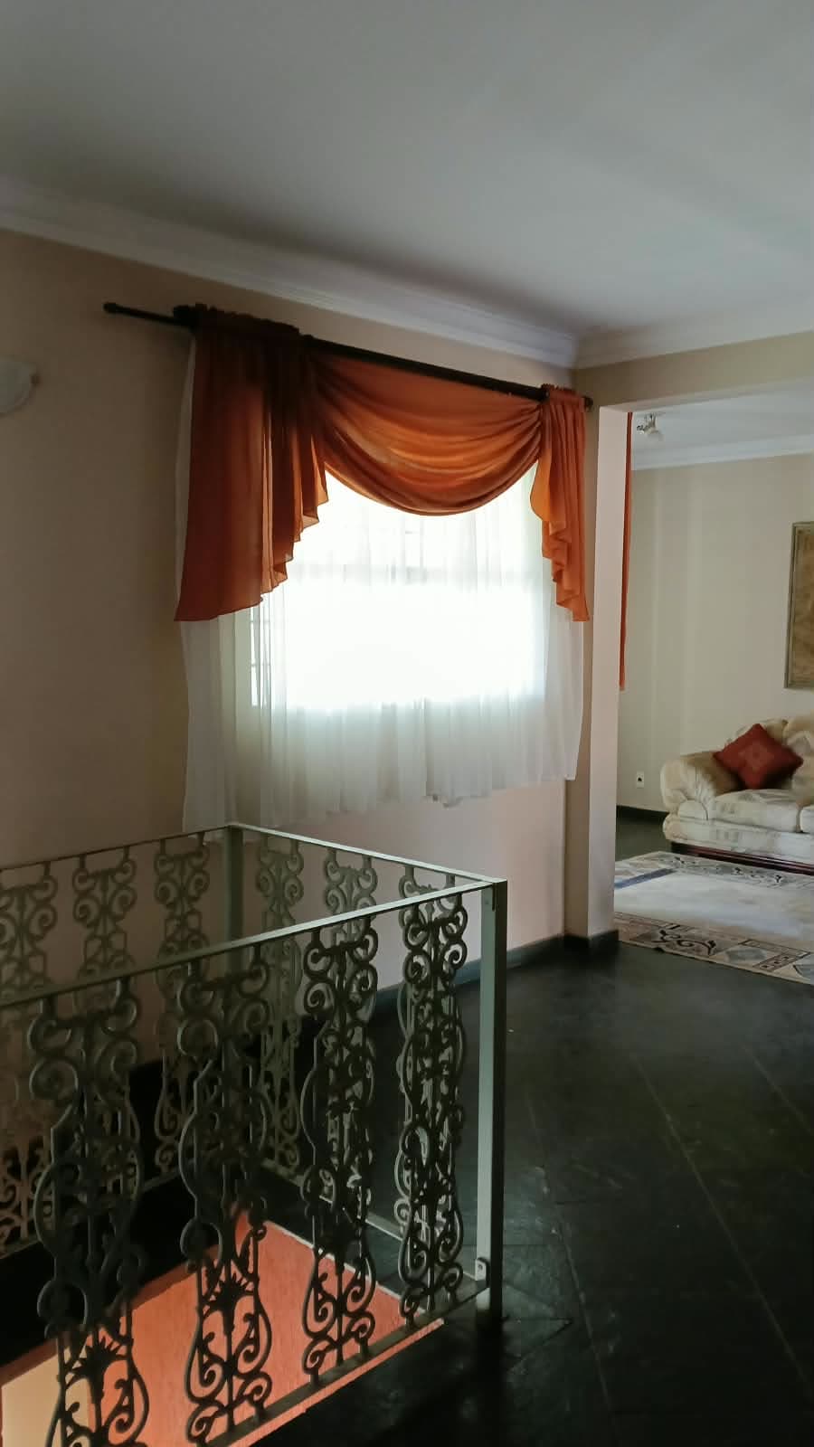 O mezanino do segundo andar, com o guarda-corpo de ferro, a cortina e o sofá da sala ao fundo