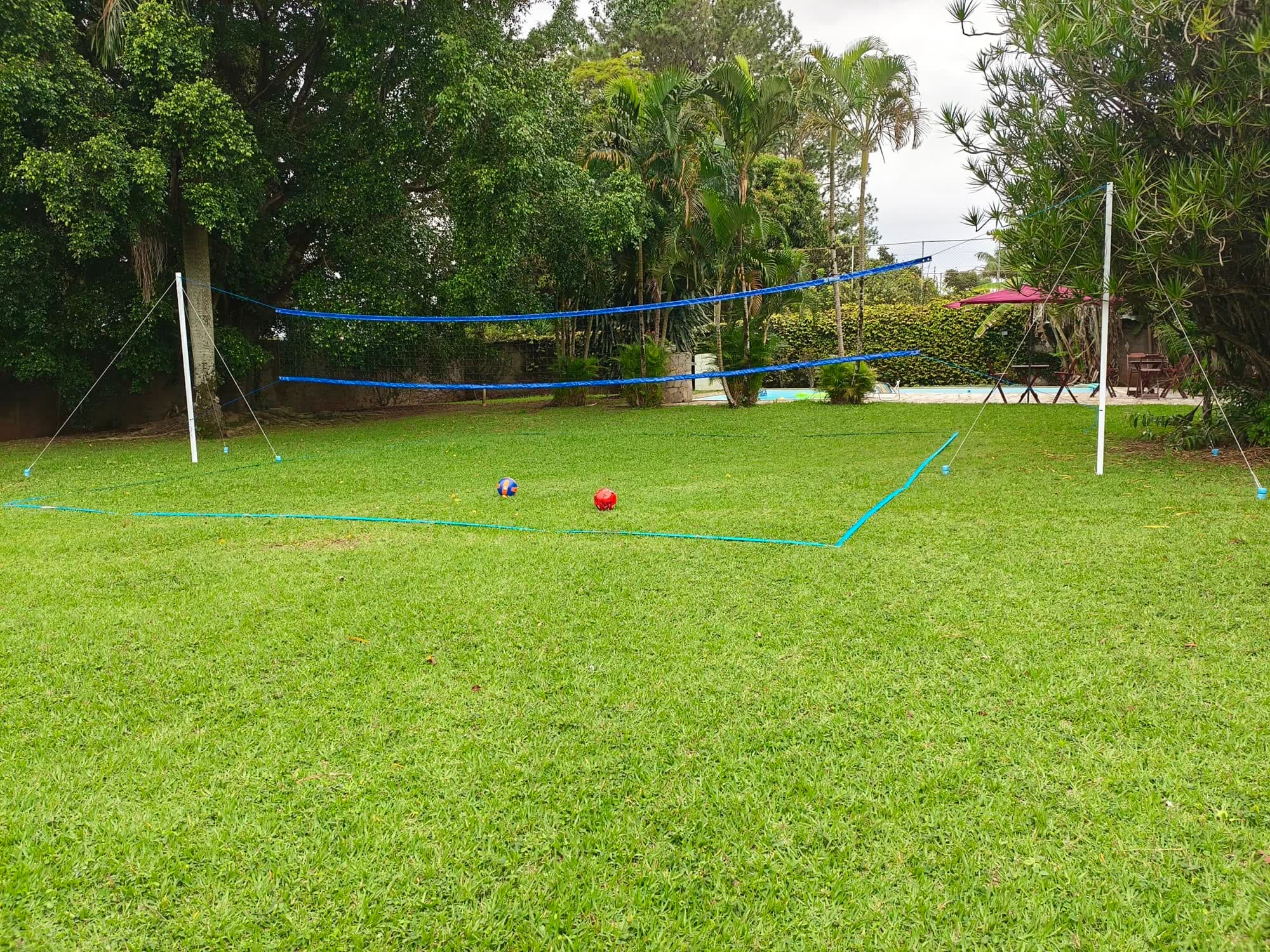 A quadra de vôlei montada no gramado, com as bolas e a piscina ao fundo