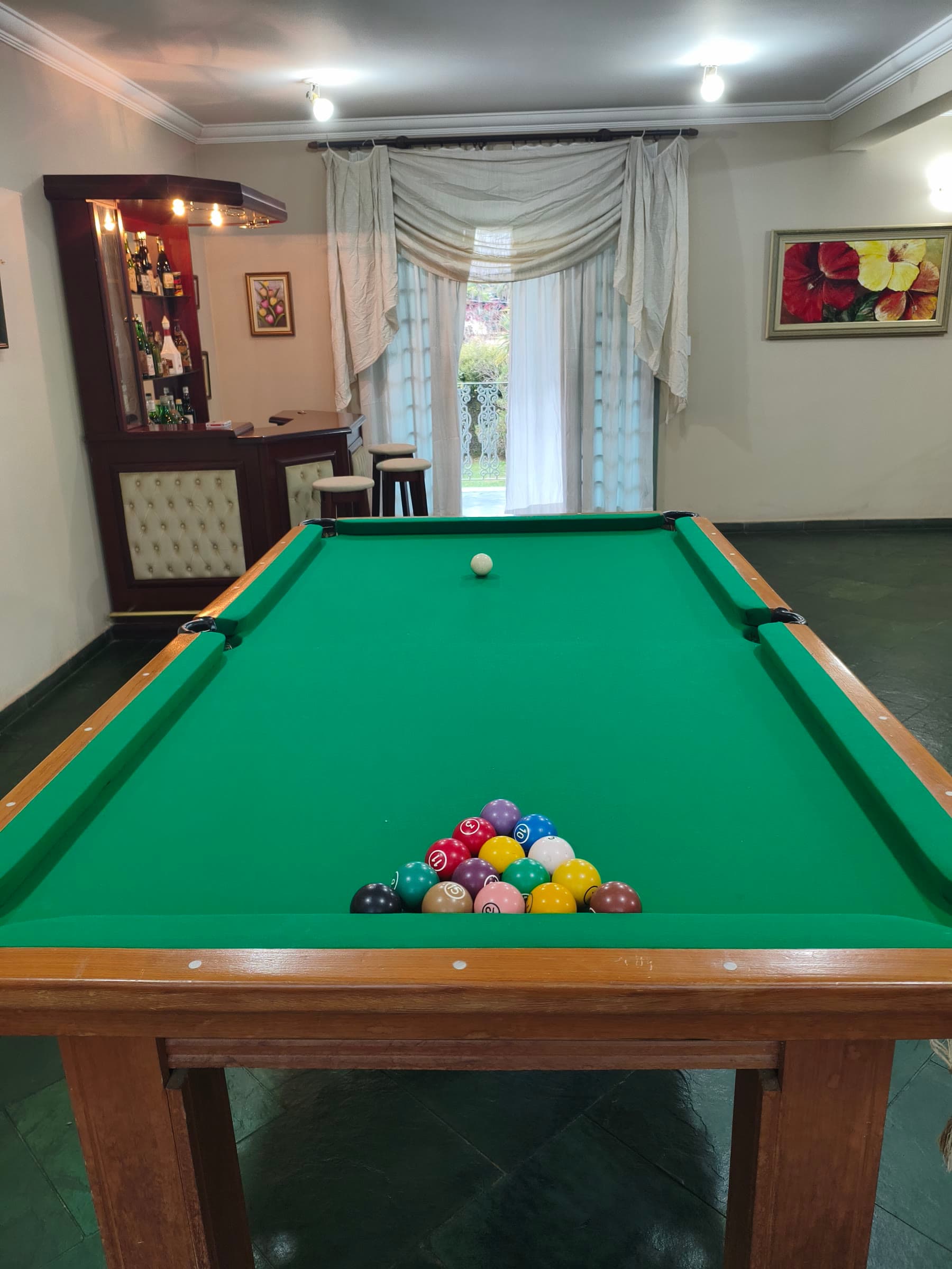 A sinuca com as bolas armadas, o bar com banquetas e a porta para a varanda