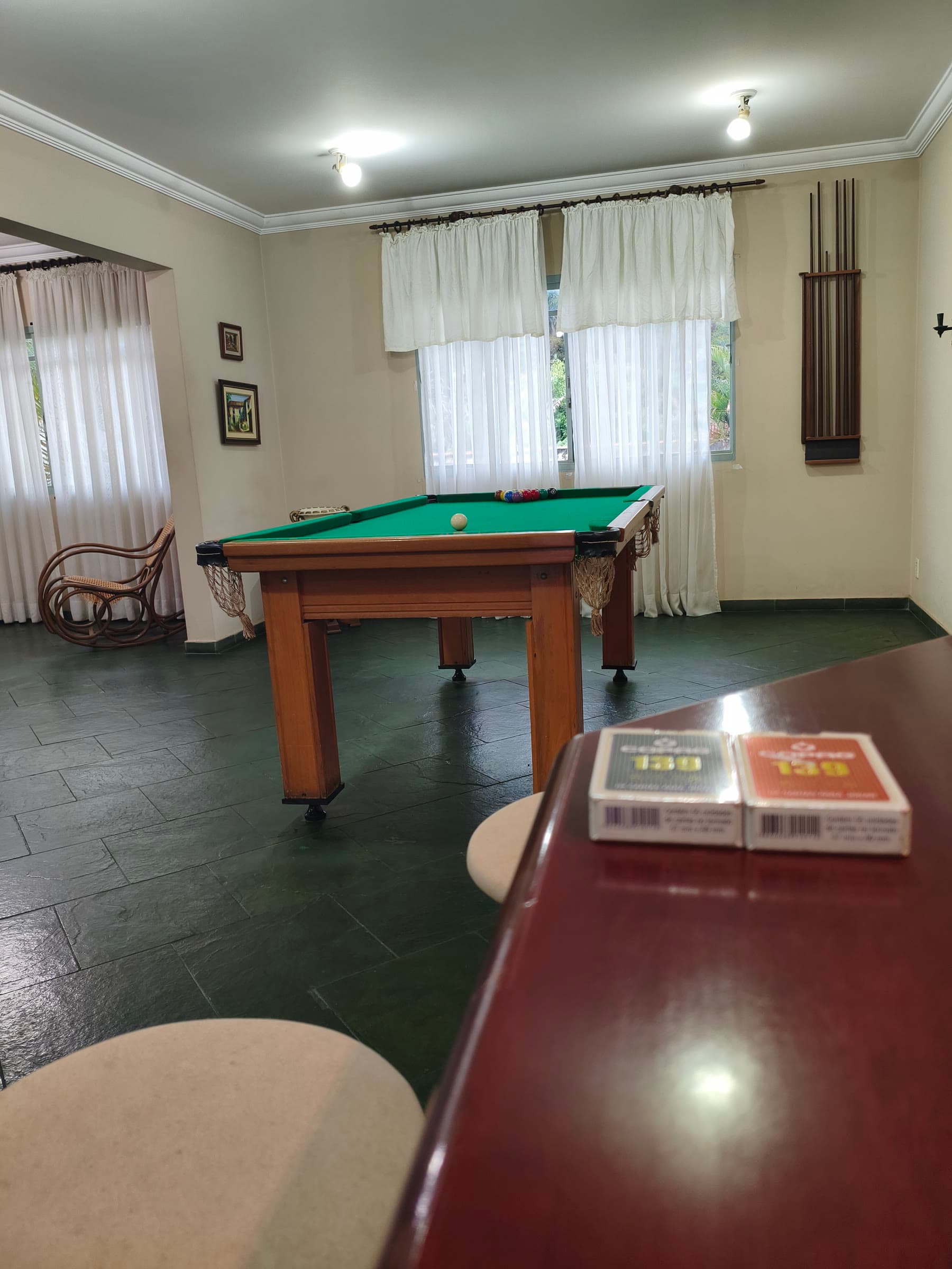 O salão de jogos visto do bar: dois baralhos no balcão, a sinuca e a cadeira de balanço